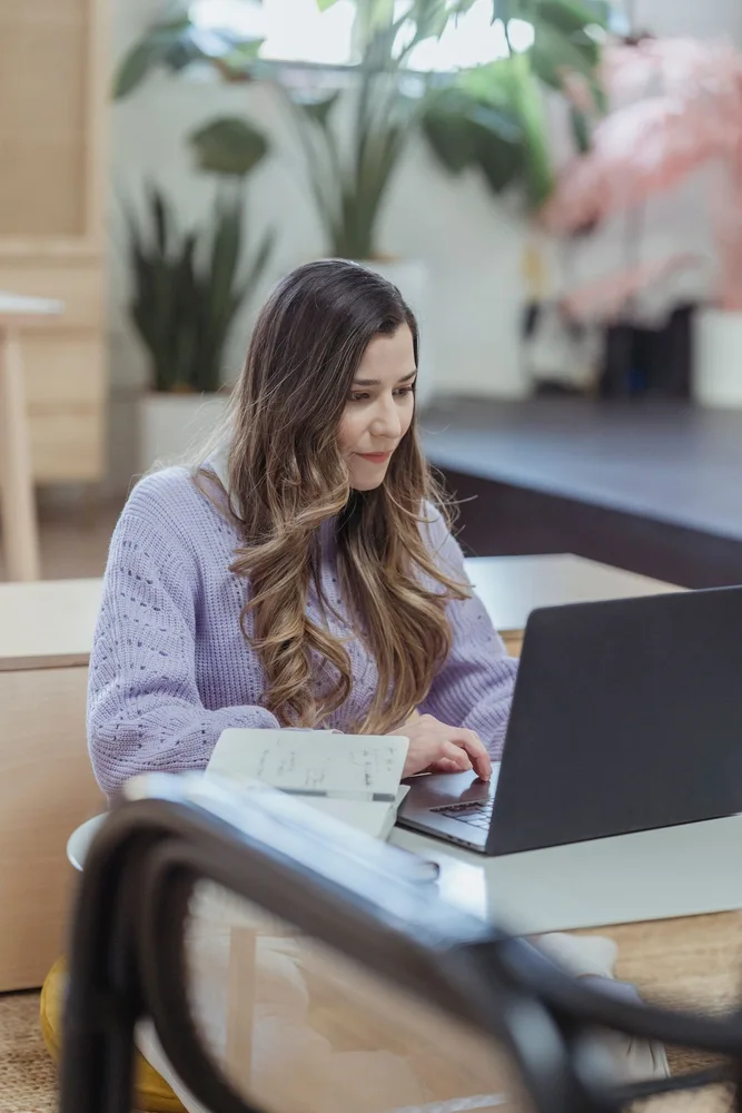 A woman working on a laptop beside an open notebook