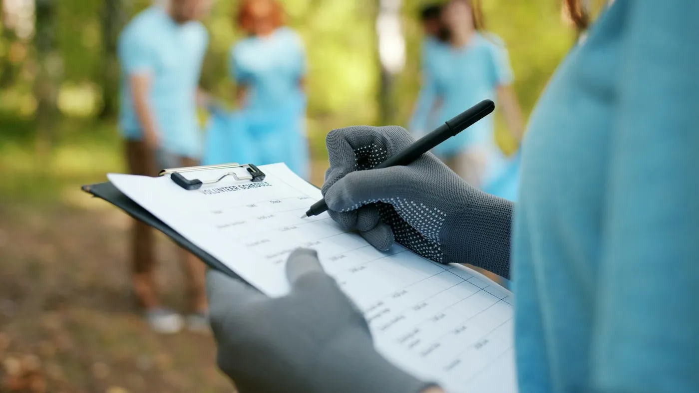 A volunteer records notes while a group works outdoors